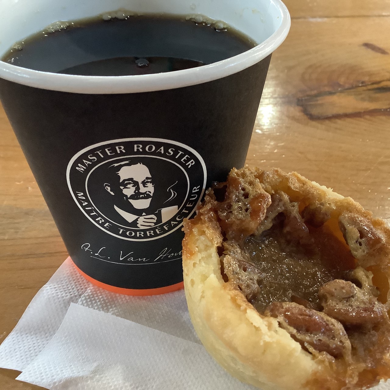 Van Houtte coffee cup filled with black coffee with a pecan butter tart leaning on it.