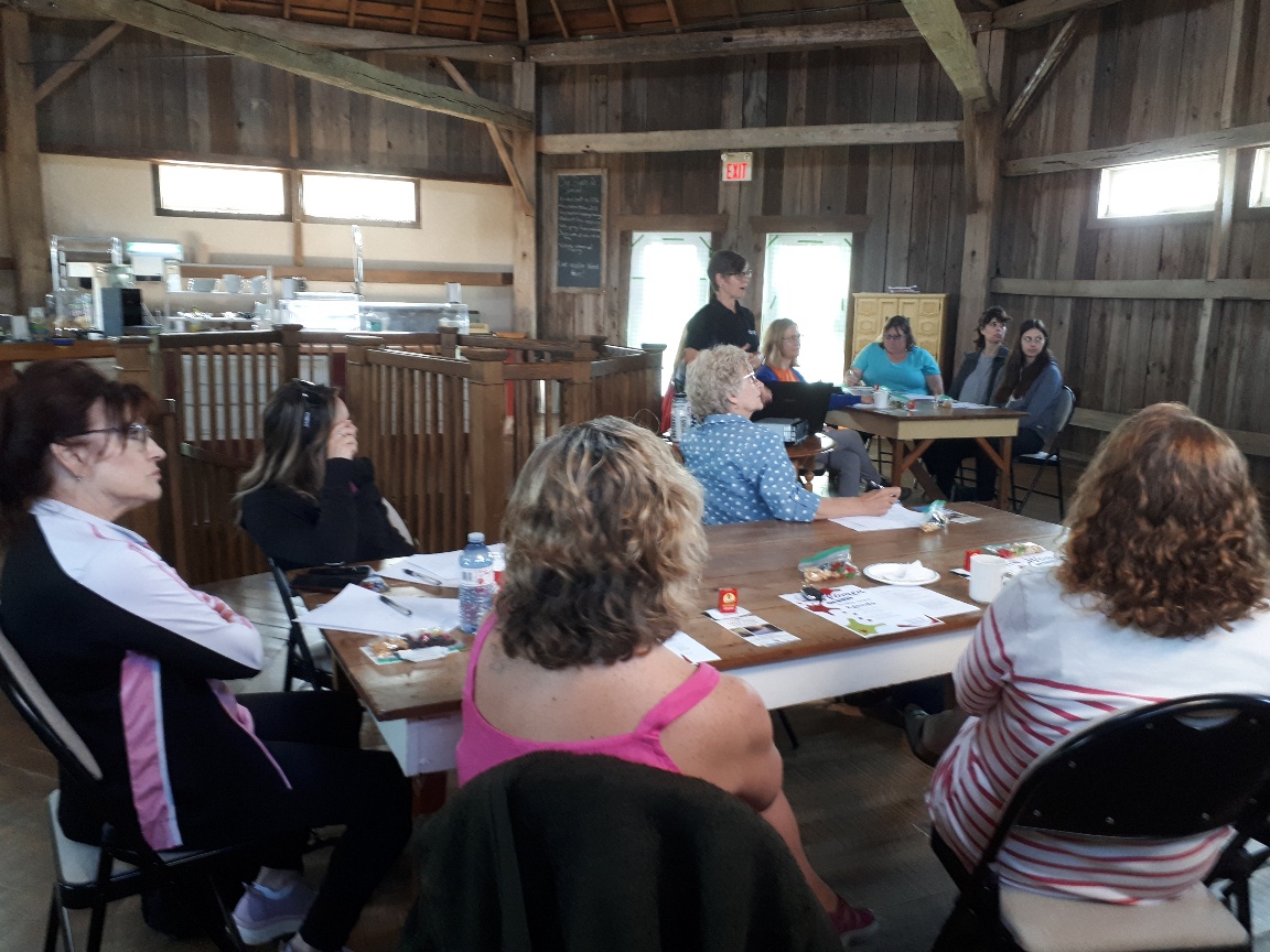 Back Road Cycling tours and clinics in southwestern Ontario host regular cycling skill development clinics.  A group of women sit at two long tables listening to a speaker.